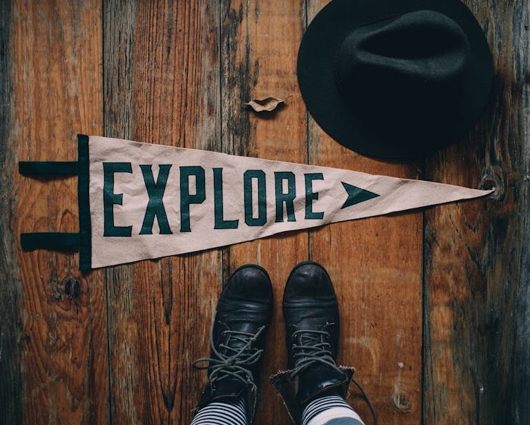 A pair of vintage boots next to a hat and a decorative banner with 'Explore' on a wooden floor.