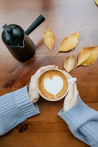 A serene autumn scene with hands holding latte and heart-shaped art.