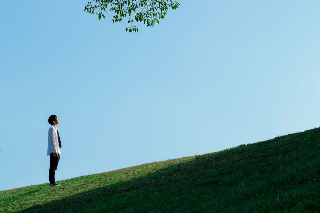 Adult male looking up while standing on a grassy hill under a clear sky.