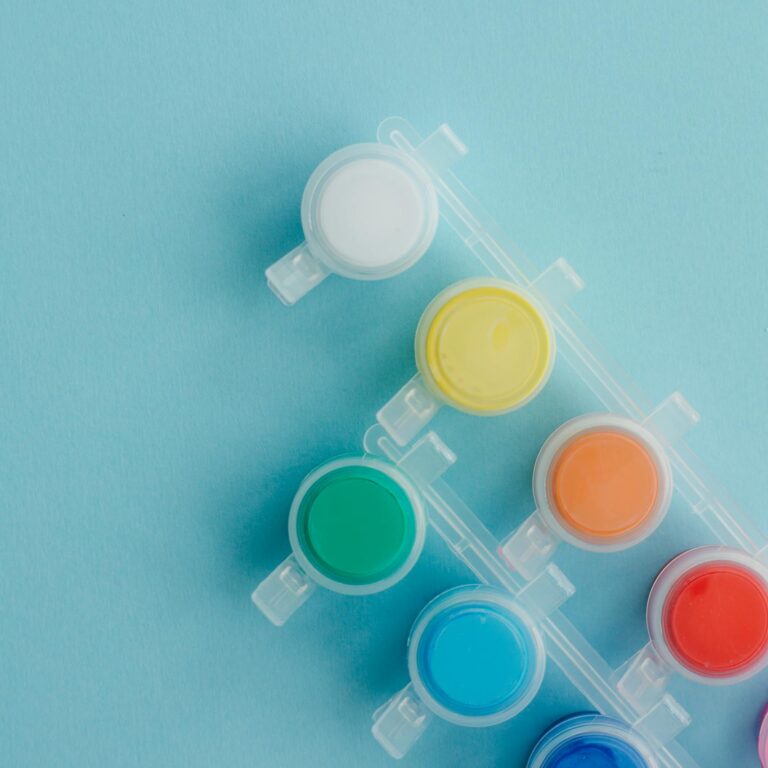 Overhead view of assorted colorful paints arranged on a blue surface, ideal for creative projects and art themes.